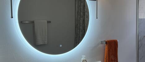 A bathroom with a round mirror, two wall-mounted lights, a white sink, and a towel rack.