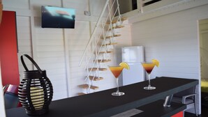 En bardisk med en svart skiva, två drinkar med apelsinskivor, en svart, flätad korg och en tv som är monterad på väggen.