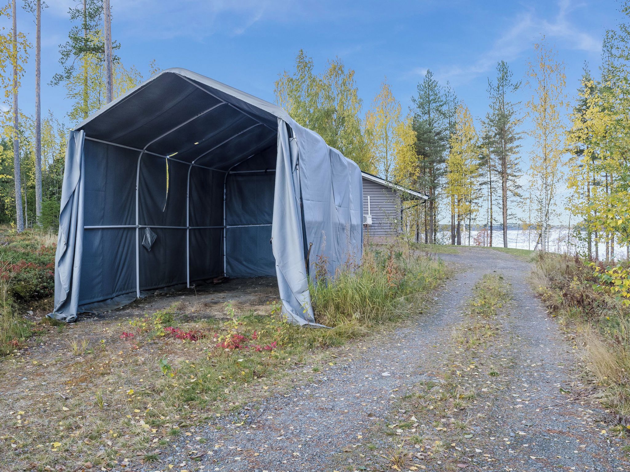 A covered structure with a gravel path leading to it, surrounded by trees and a body of water.