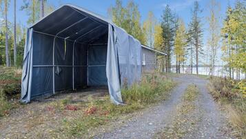 A covered structure with a gravel path leading to it, surrounded by trees and a body of water.