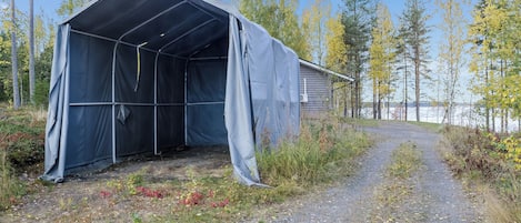 A covered structure with a gravel path leading to it, surrounded by trees and a body of water.
