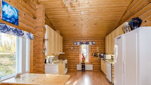 L’intérieur d’une cabane en rondins, avec des murs en bois, une table à manger en bois et un coin cuisine doté d’appareils électroménagers blancs.