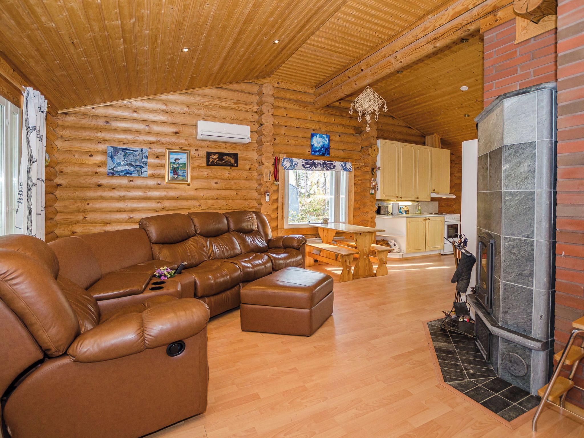 A cozy log cabin interior with a leather sofa, a dining table, and a stone fireplace.