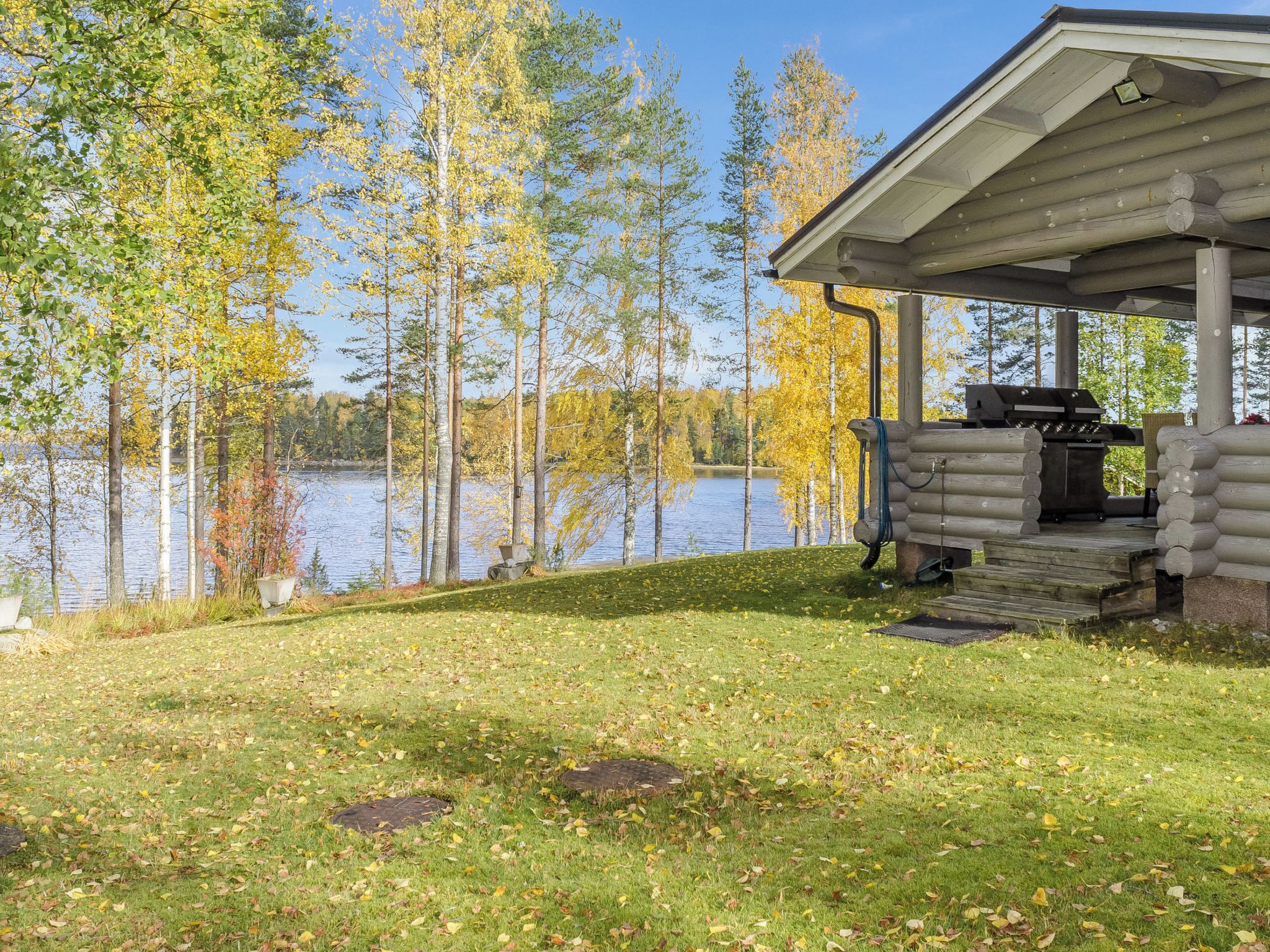 Järvenrantahuvila, jossa on katettu kuisti, grilli ja näkymä järvelle.