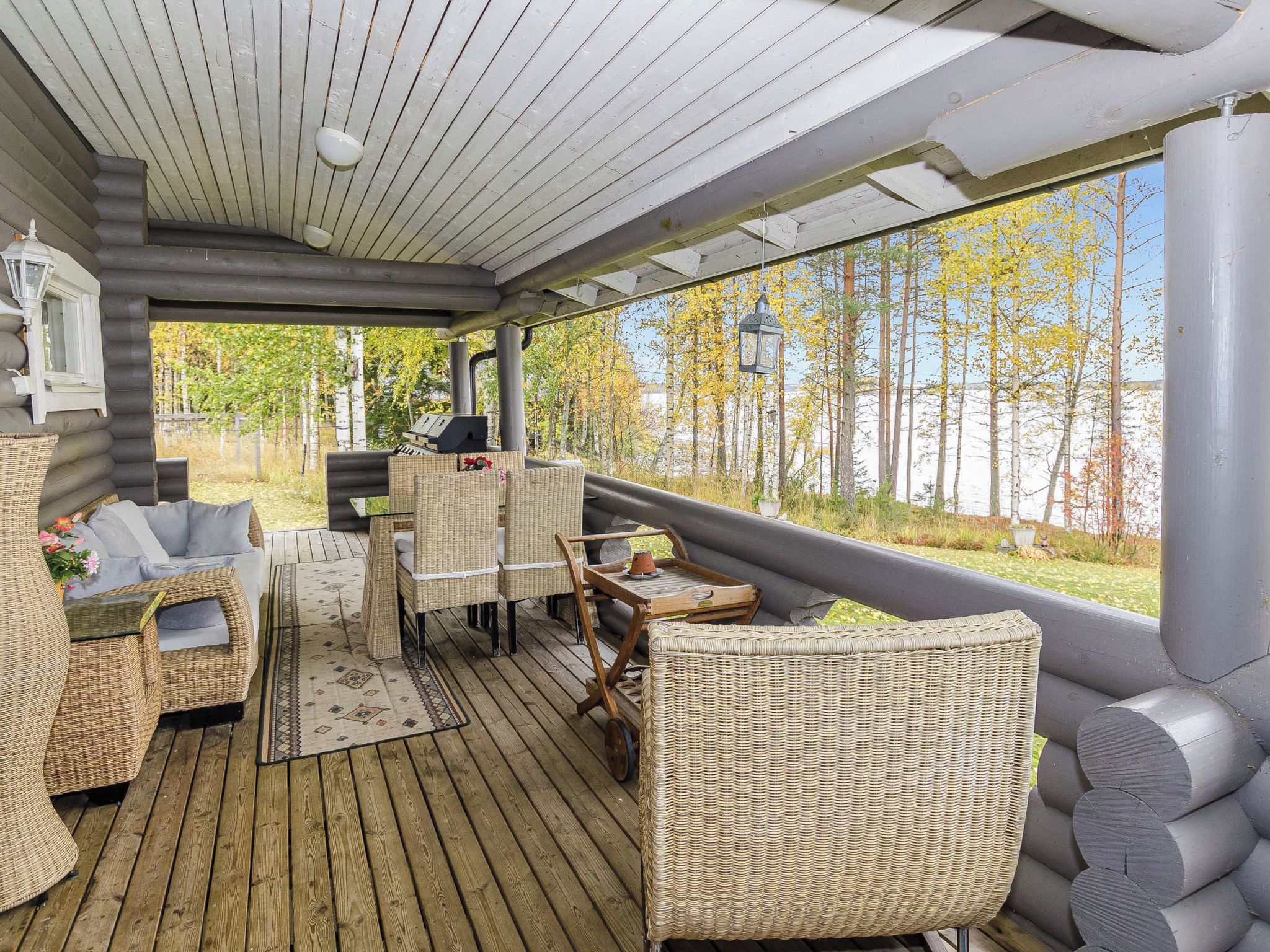 A covered outdoor seating area with wicker furniture, a grill, and a view of trees.