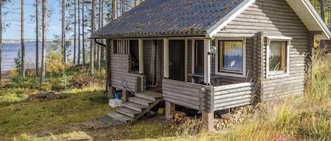 Une cabane en rondins avec une véranda, une cheminée et une vue sur l’eau.