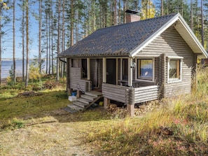 A log cabin with a porch, a chimney, and a view of the water.
