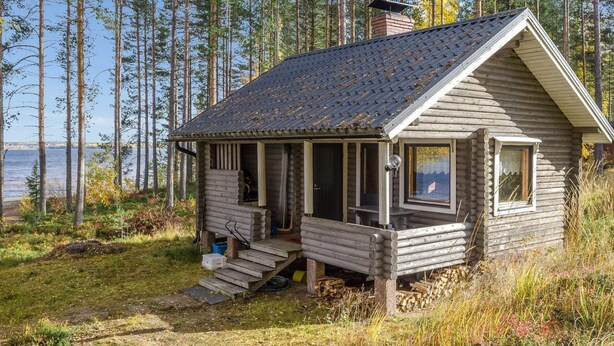 Une cabane en rondins avec une véranda, une cheminée et une vue sur l’eau.