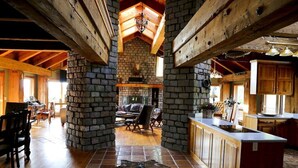 A rustic interior with exposed wooden beams, a stone fireplace, a dining area, and a kitchen with wooden cabinets. - Luxury Ranch Compound on 300 acres, just outside Galena Territory. 30 bedrms. (Elizabeth)