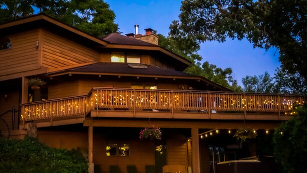 A two-story wooden house with a balcony adorned with string lights, a covered porch, and a chimney. - Luxury Ranch Compound on 300 acres, just outside Galena Territory. 30 bedrms. (Elizabeth)