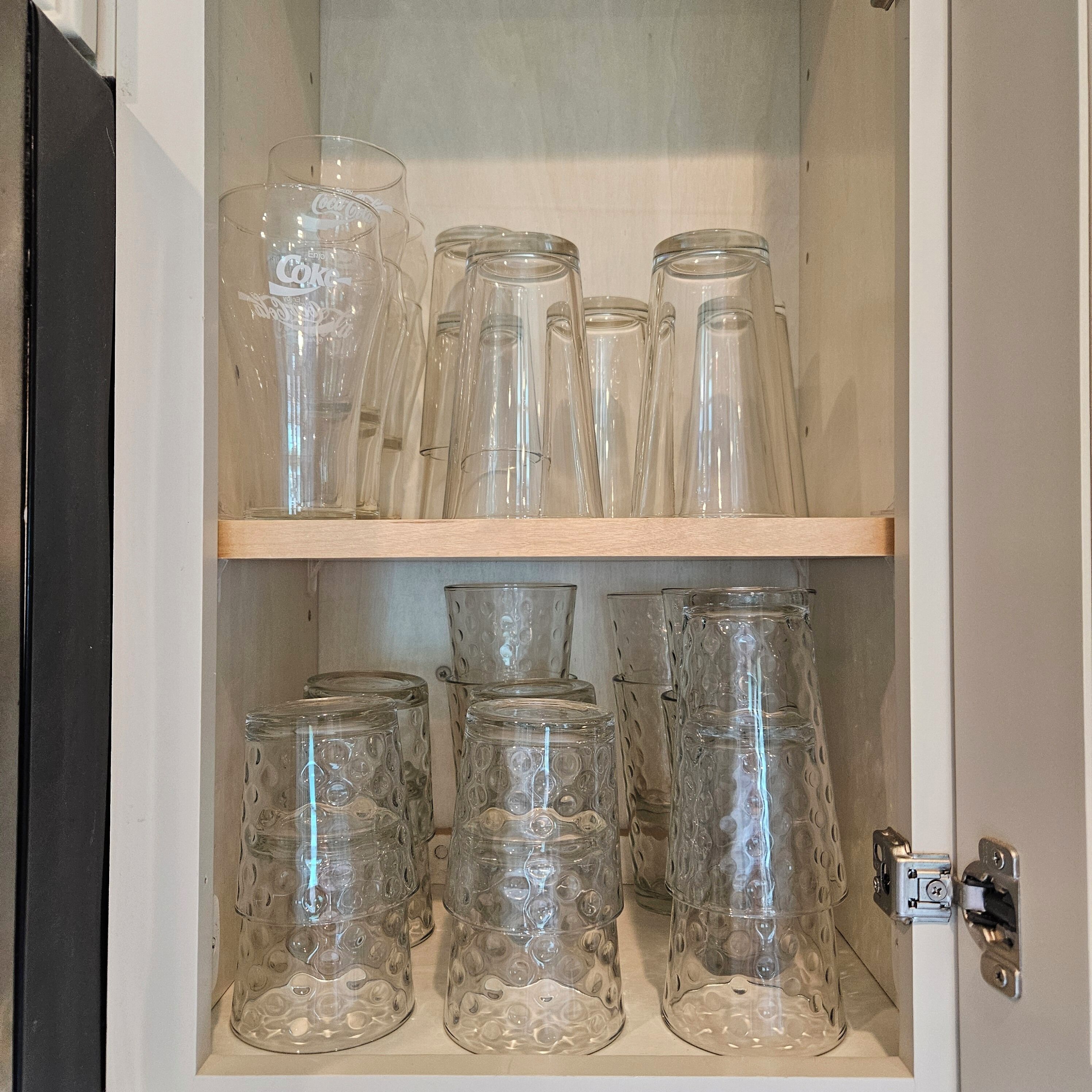 A cabinet with two shelves containing clear glass bottles and glasses.