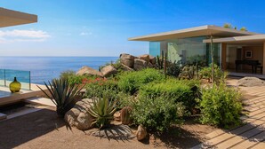 Una villa moderna con veranda in vetro, patio con piante tipiche del deserto e vista sul mare.