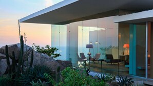 Una casa moderna con facciata in vetro, un patio con sedie e vista sul paesaggio desertico.