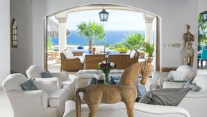 A living room with white sofas, a wooden horse sculpture, and a view of the ocean through an arched doorway. - 2 FREE NIGHTS IN CABO at Villa Buena Vida! (Cabo Corridor)