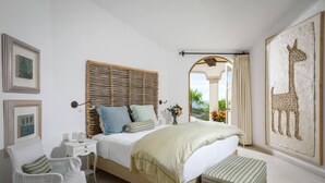 A bedroom with a bed, a nightstand, a chair, a bench, and a large giraffe artwork. - 2 FREE NIGHTS IN CABO at Villa Buena Vida! (Cabo Corridor)