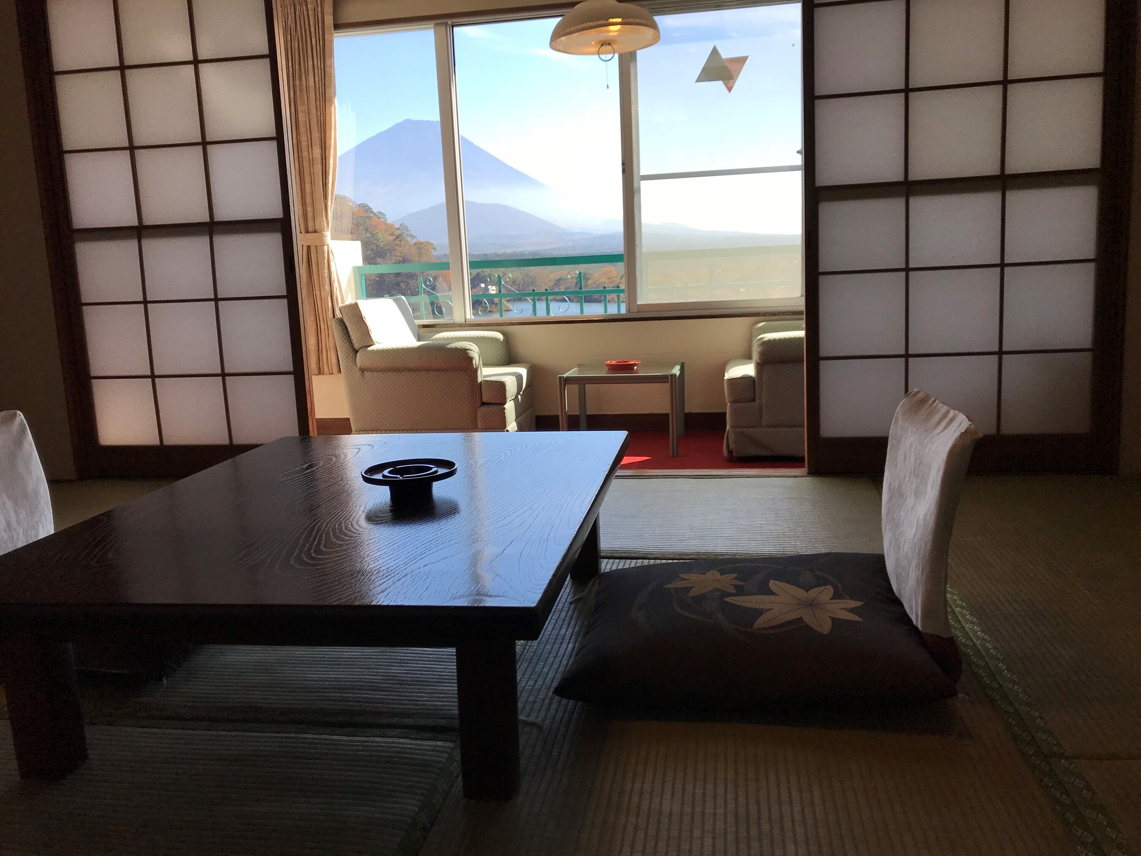 Una habitación japonesa tradicional con suelo de tatami, una mesa baja y vistas a la montaña a través de amplios ventanales.