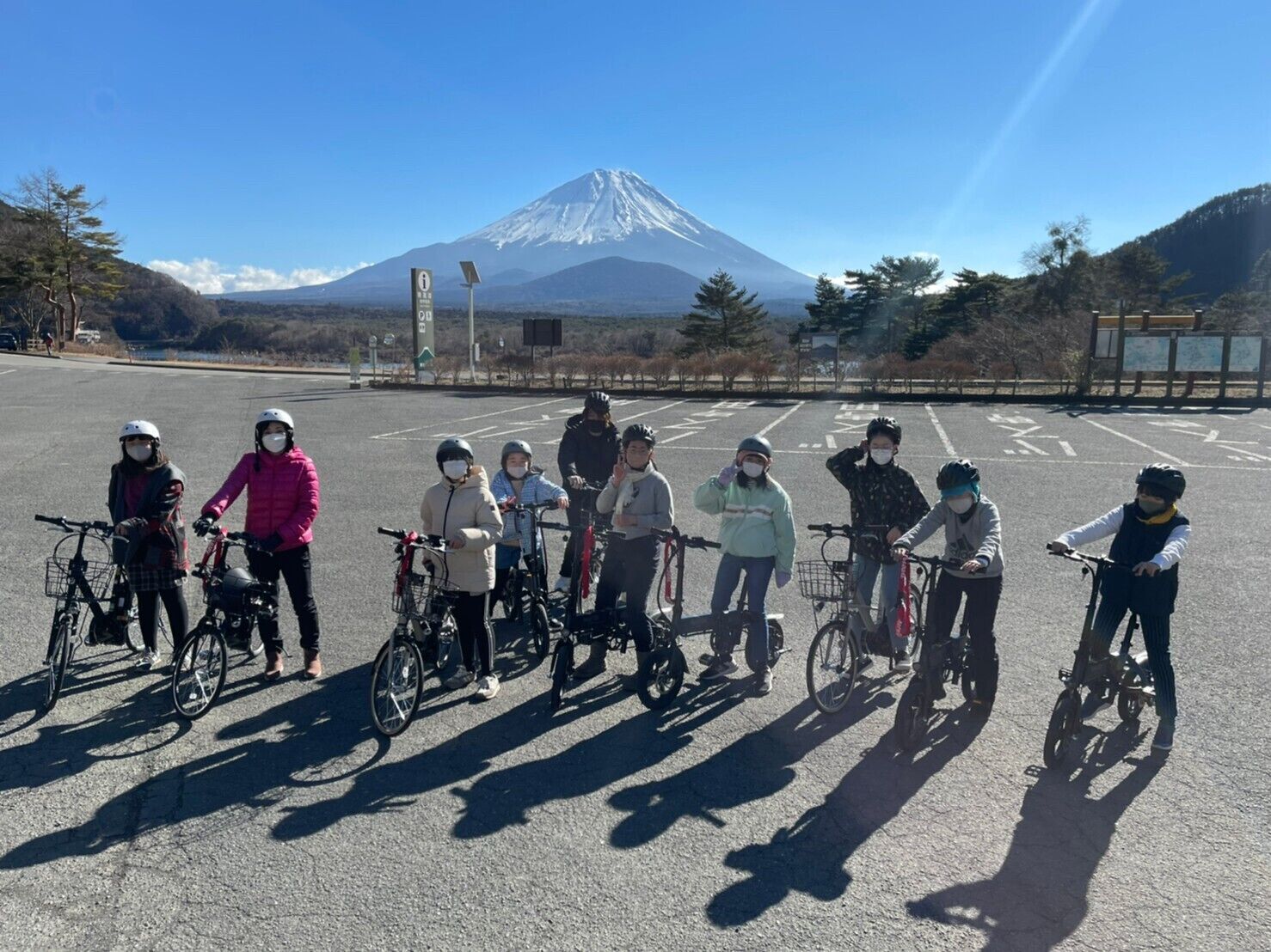 A group of people with bicycles in a parking lot with a mountain in the background.