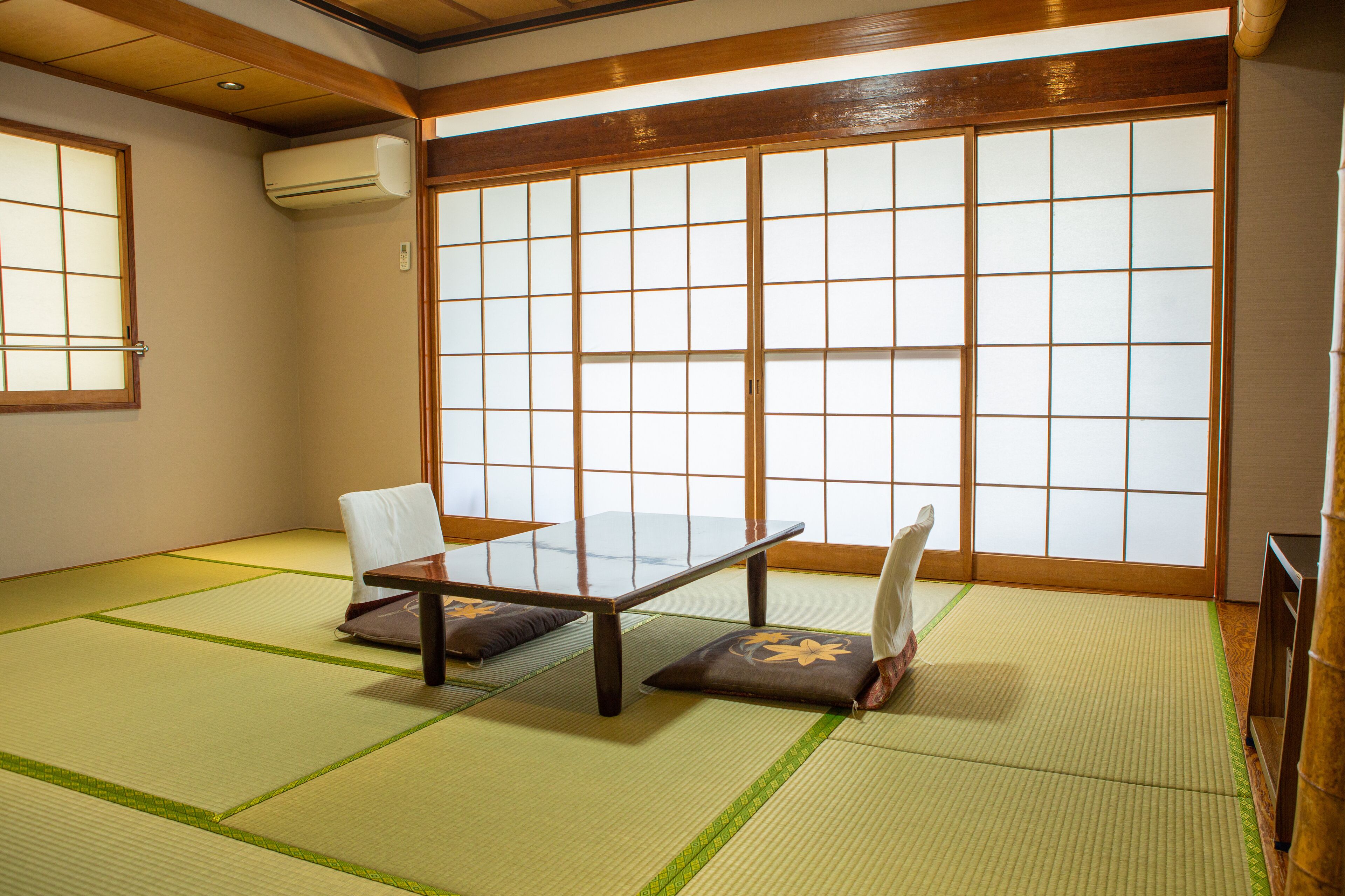 A tatami mat room with a low table and cushions, large shoji screens, and a sliding door.