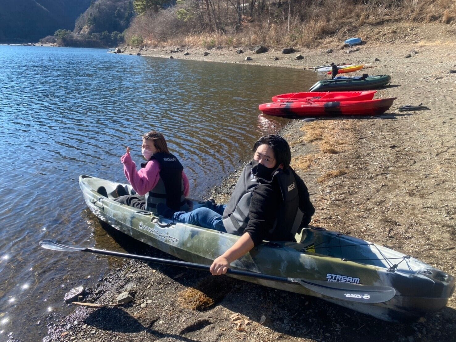 Two people in a kayak on a calm riverbank.