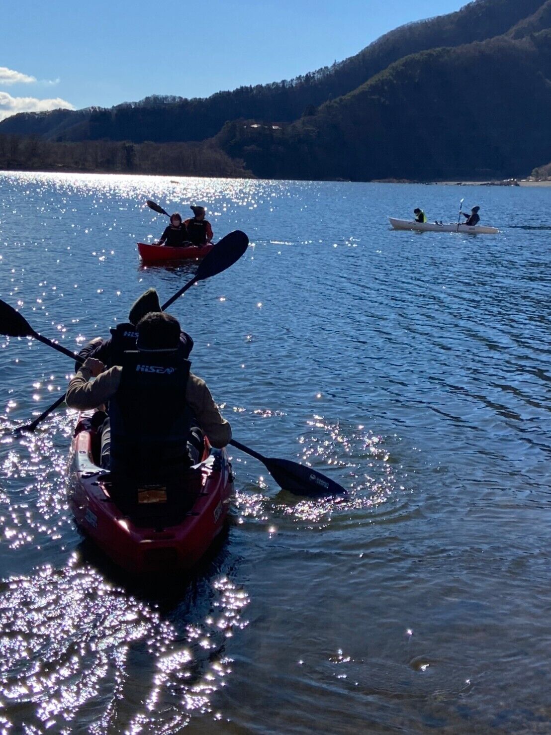 A kayaker in a red kayak on a calm lake with mountains in the background.