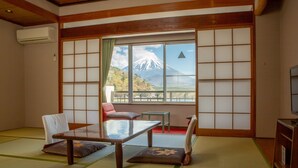 A traditional Japanese room with tatami flooring, a low table, and cushions. A large window offers a view of a mountain. - Shoji Lake Hotel (Fujikawaguchiko)