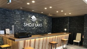 A reception desk with a stone wall backdrop, a clock, and a laptop. - Shoji Lake Hotel (Fujikawaguchiko)
