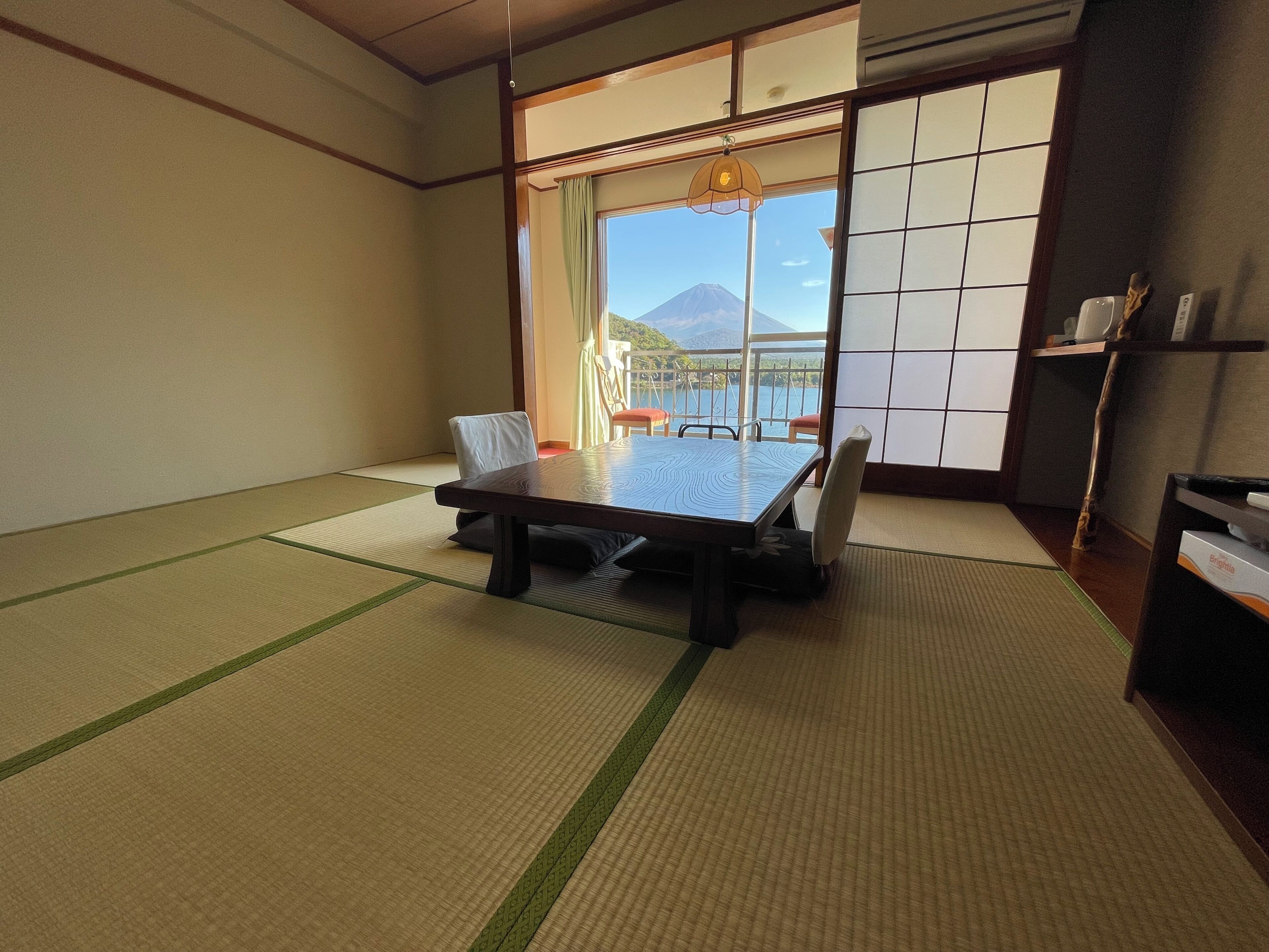 A traditional Japanese room with tatami flooring, a low table, and a view of a mountain through large shoji doors.