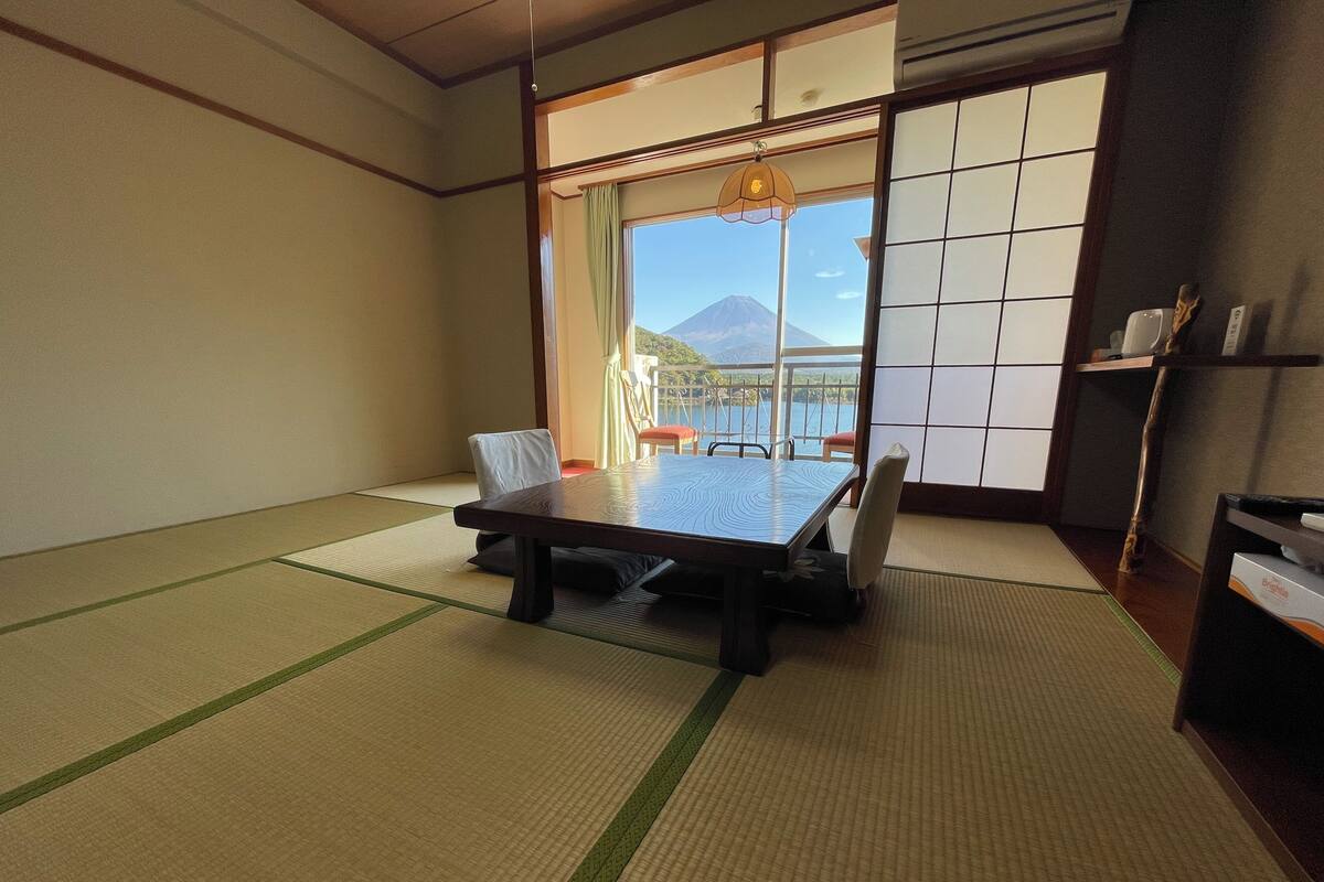 Una habitación tradicional japonesa con suelo de tatami, una mesa baja y vistas a la montaña a través de grandes puertas shoji.