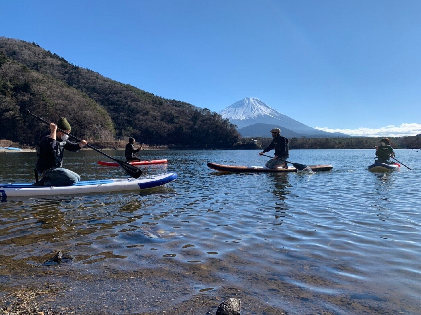 En gruppe mennesker padler på stand-up paddleboards på en rolig sø med et bjerg i baggrunden.
