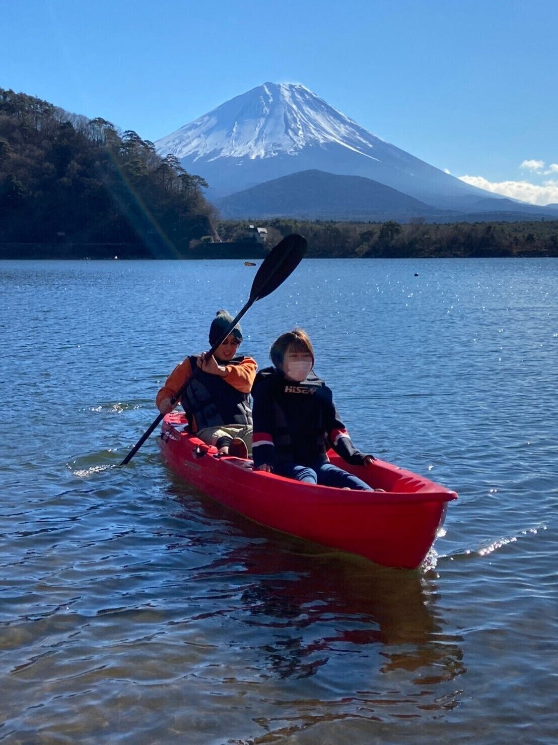 Dos personas en un kayak rojo en un lago tranquilo, con una montaña al fondo.