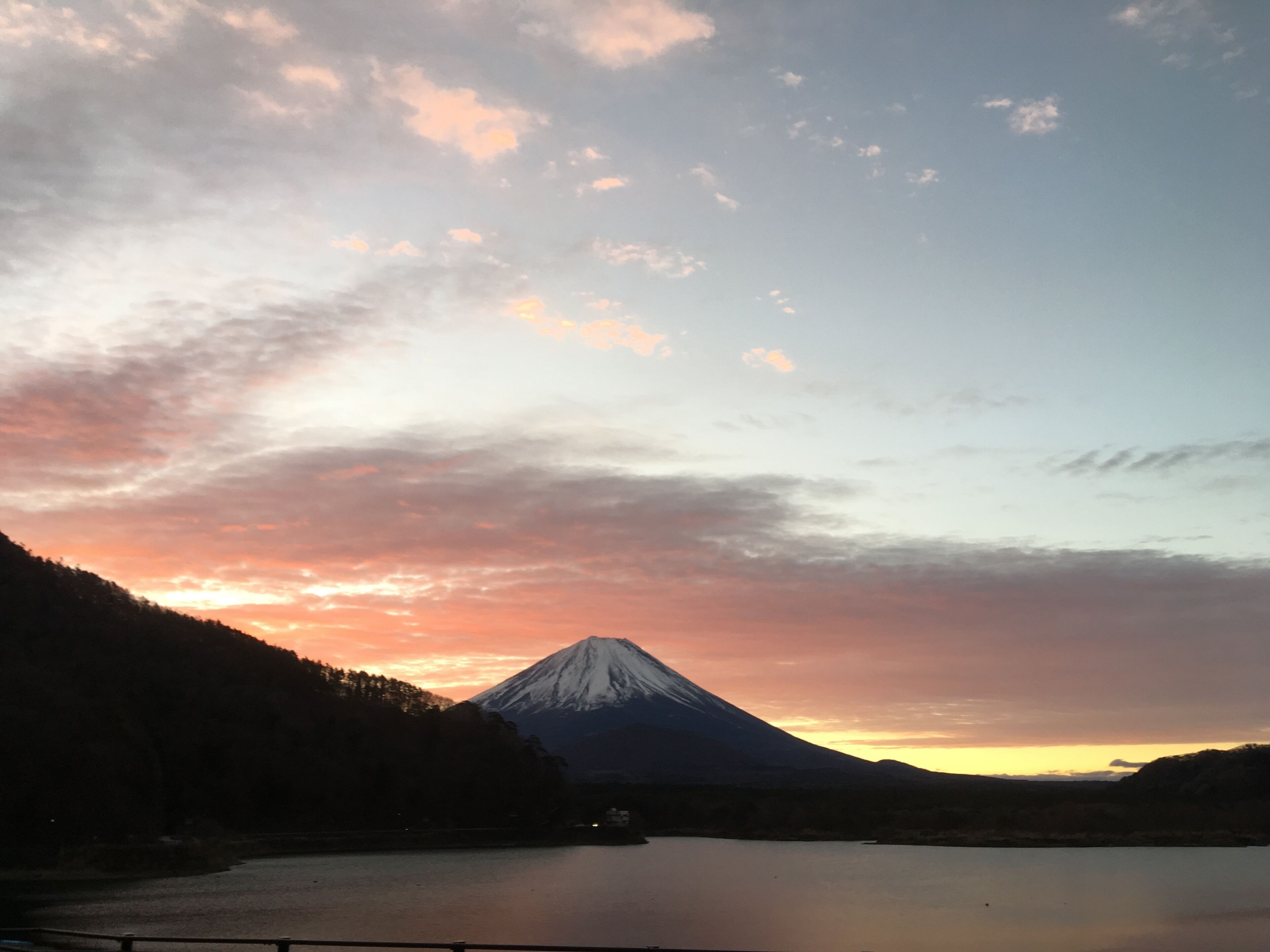 Una montaña con un lago en primer plano y un atardecer de fondo.