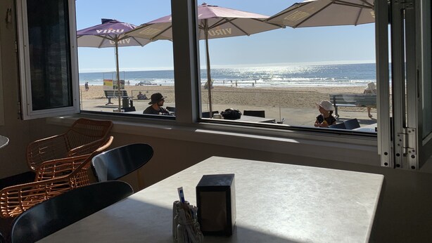 Een restaurant aan het strand met grote ramen, met uitzicht op het strand en de oceaan.
