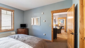 A bedroom with a bed, a TV, a dresser, and a door leading to a bathroom.