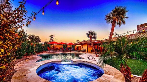 A hot tub surrounded by a pool, palm trees, and outdoor seating.