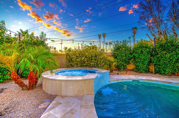 Piscina com hidromassagem, cercada por vegetação exuberante e céu claro.