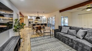 A modern living room with a grey sofa, a patterned rug, and a dining area with a table and chairs.