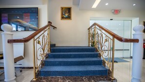Eine Treppe mit blauen Teppichstufen und goldenen Geländern, die zu einer höheren Etage führt.