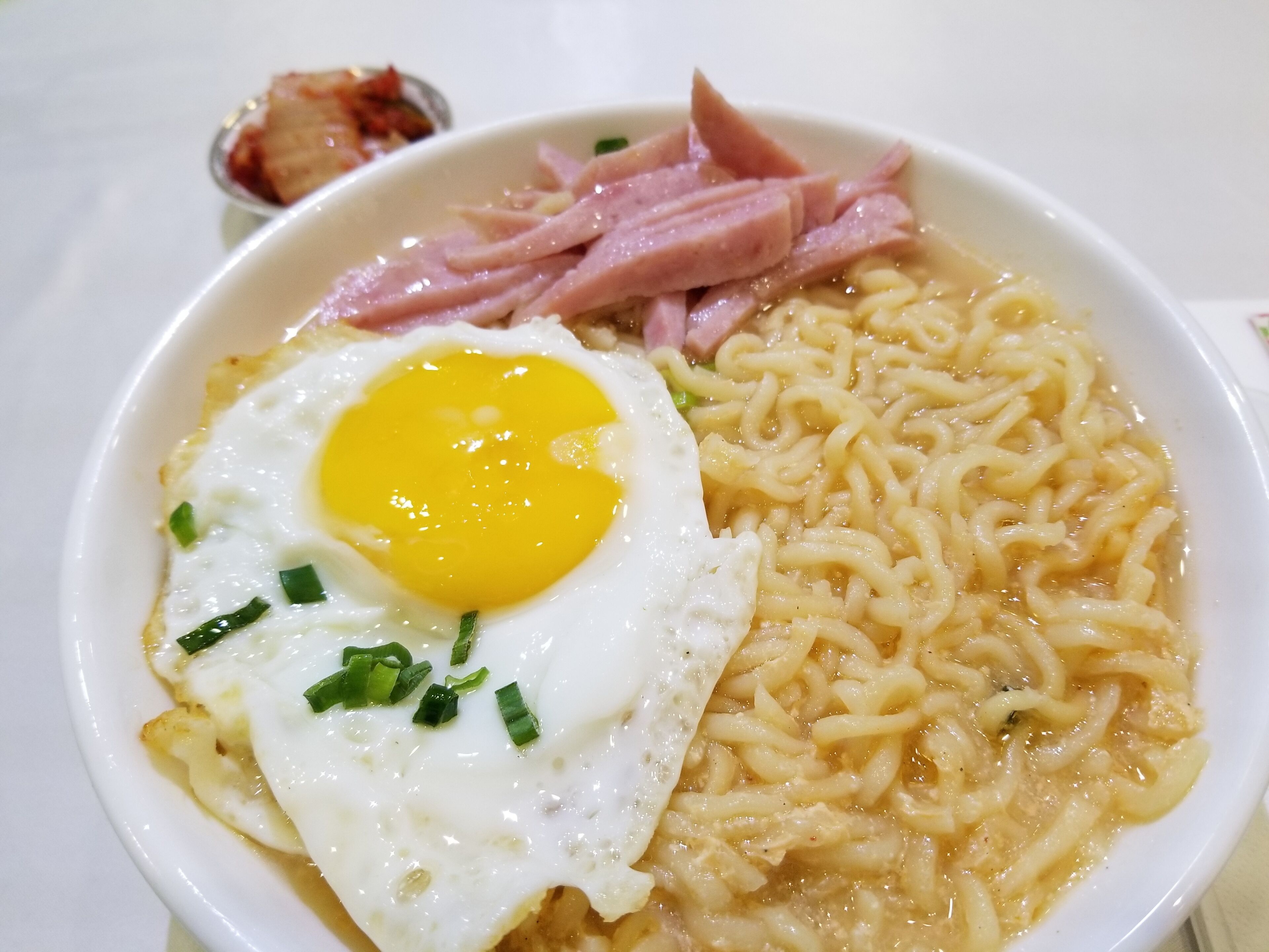 Un tazón de ramen con un huevo frito, jamón en rodajas y cebolletas picadas.