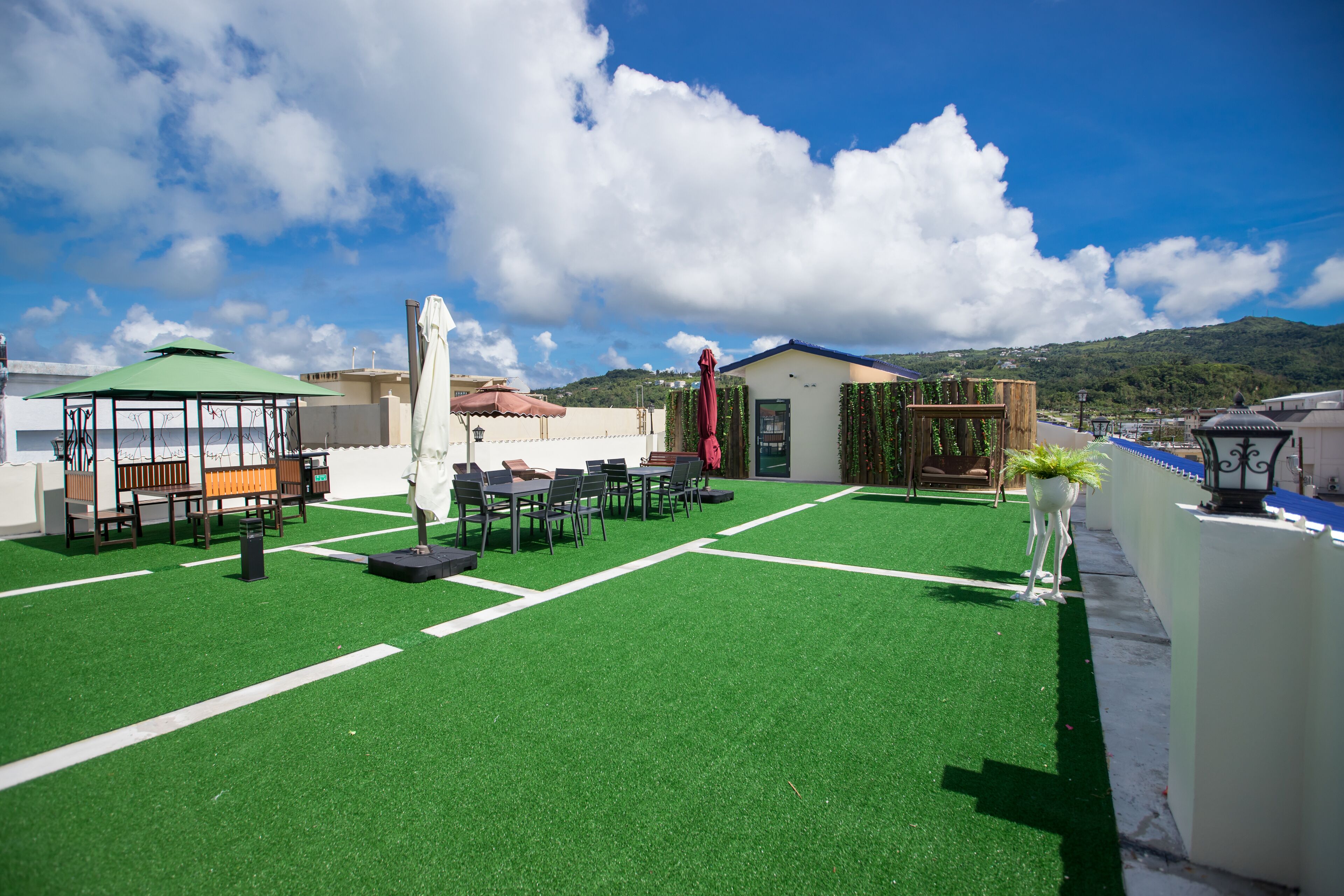A rooftop terrace with green artificial turf, outdoor seating, and a view of a mountain.