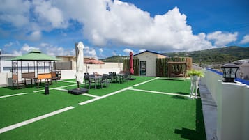 A rooftop terrace with green artificial turf, outdoor seating, and a view of a mountain.