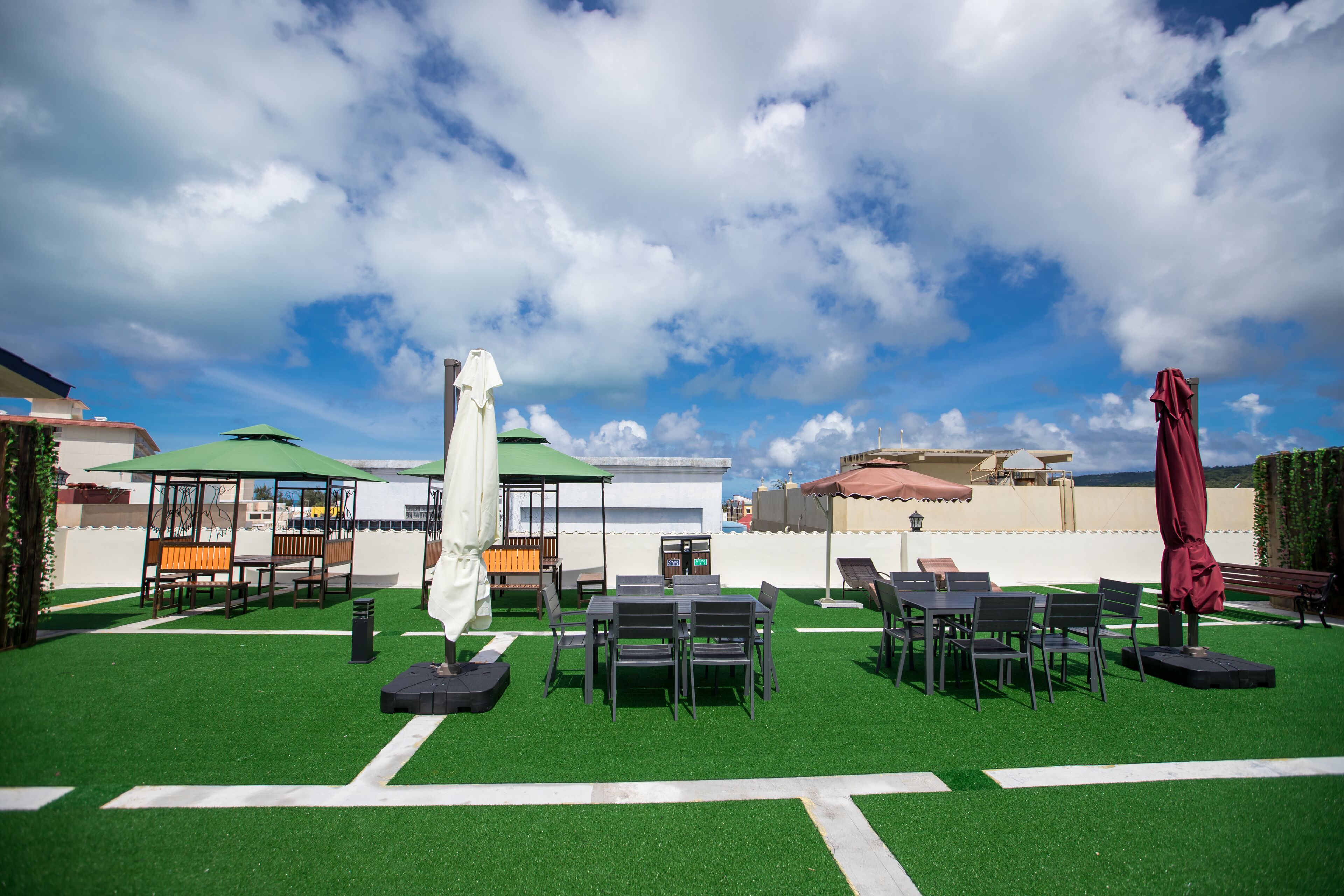 An outdoor patio area with artificial grass, tables, chairs, and umbrellas.