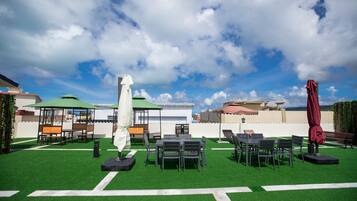 An outdoor patio area with artificial grass, tables, chairs, and umbrellas.