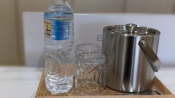 A clear bottle of water, a glass, and a stainless steel pot on a wooden tray.