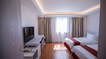 A hotel room with a TV, two beds, a desk, and a window with curtains.
