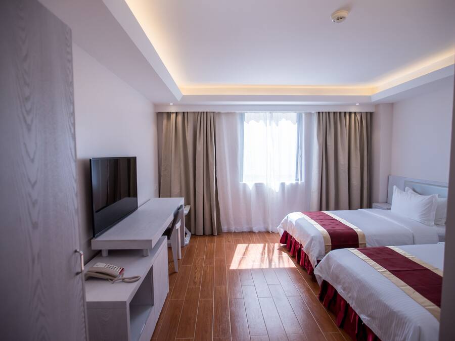 A hotel room with a TV, two beds, a desk, and a window with curtains.