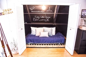 Quarto aconchegante com cama, almofadas e parede com lousa e texto.