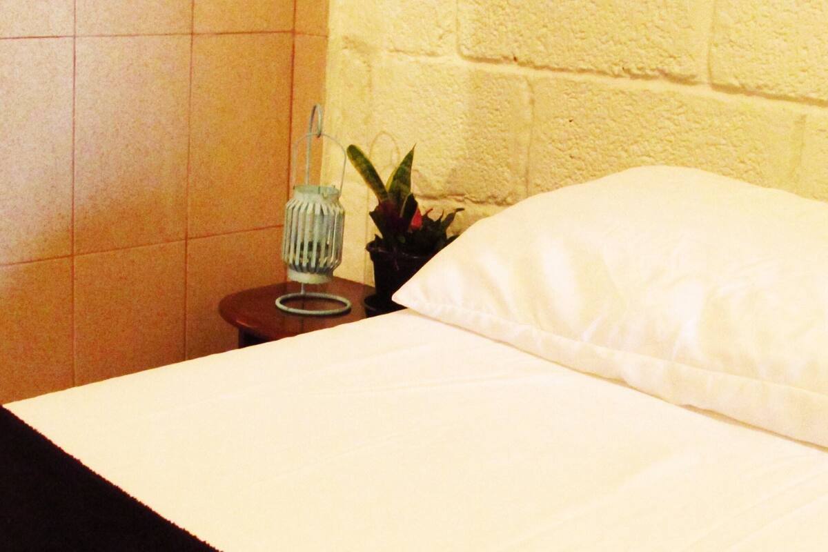 Ein Bett mit einem weißen Kopfkissen und einem kleinen Tisch daneben.