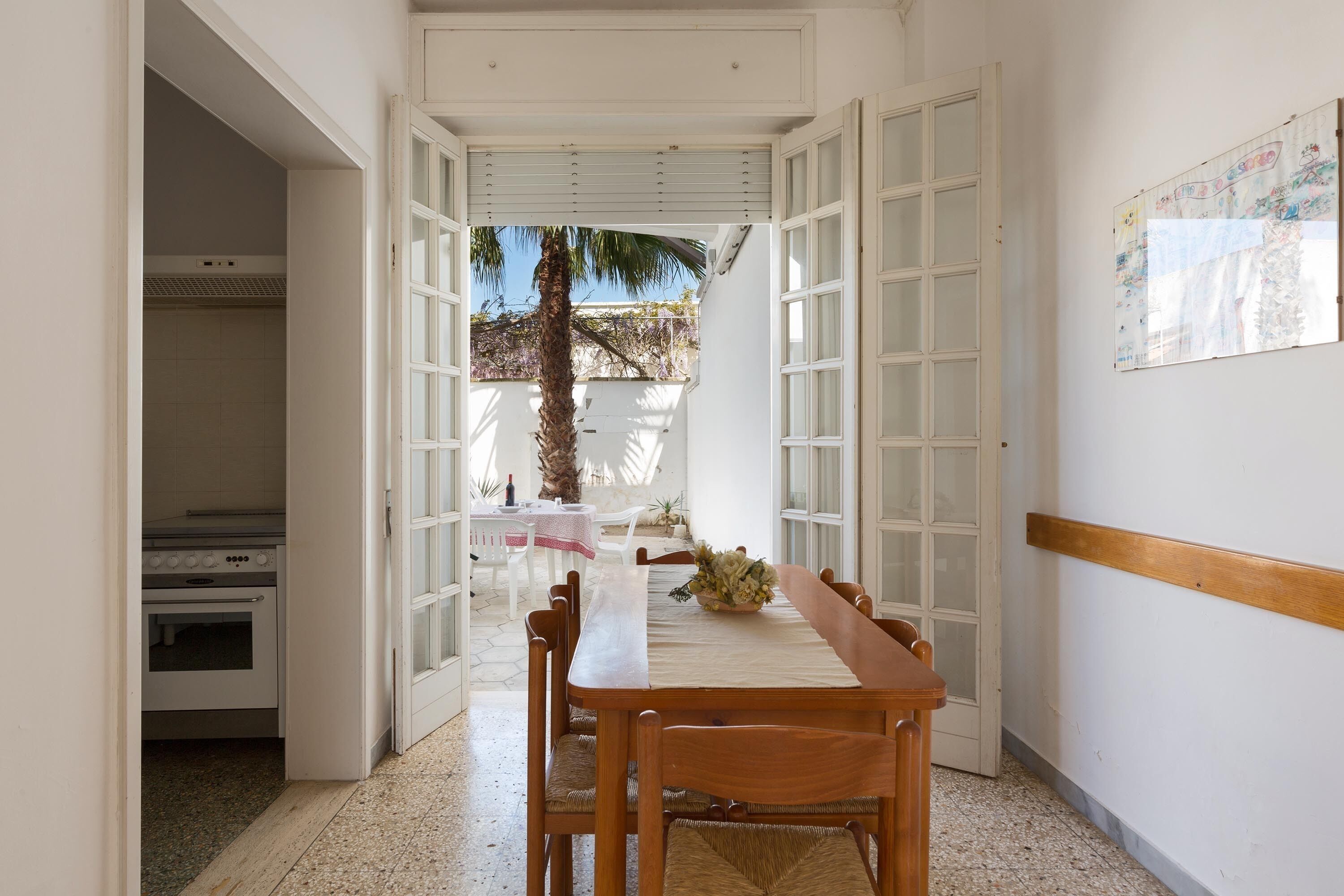 Un coin repas avec une table et des chaises, une cuisine en arrière-plan et une vue sur l’extérieur.