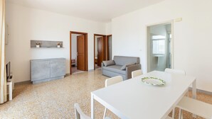 Habitació moderna i minimalista amb taula blanca, cadires, un sofà gris i un petit armari.