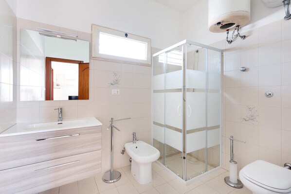 Un baño moderno con ducha de vidrio, un bidé y un tocador con espejo.